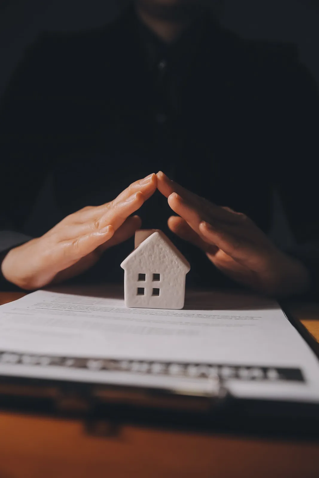 Hands forming a roof over a small model house