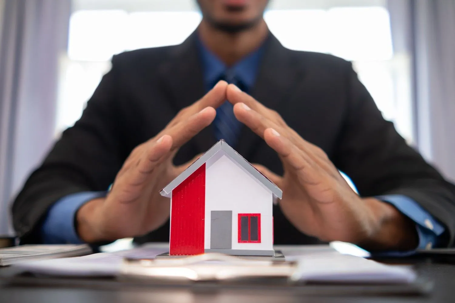 Hands held like a roof above a small model house on a desk
